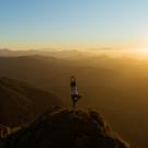 Person on a mountain standing in a yoga pose looking at the sunset