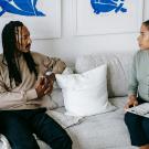 two people sitting on a light colored couch talking