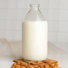 jug of almond milk with almonds spread on a white table