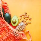 avocados and a jar of spilling almonds in an orange mesh bag against an orange background