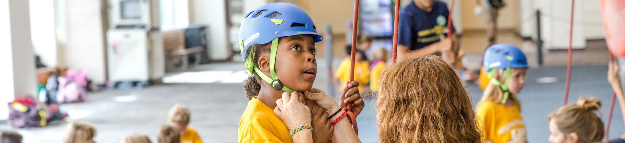 Instructor fastening rock climbing helmet to head of young student.